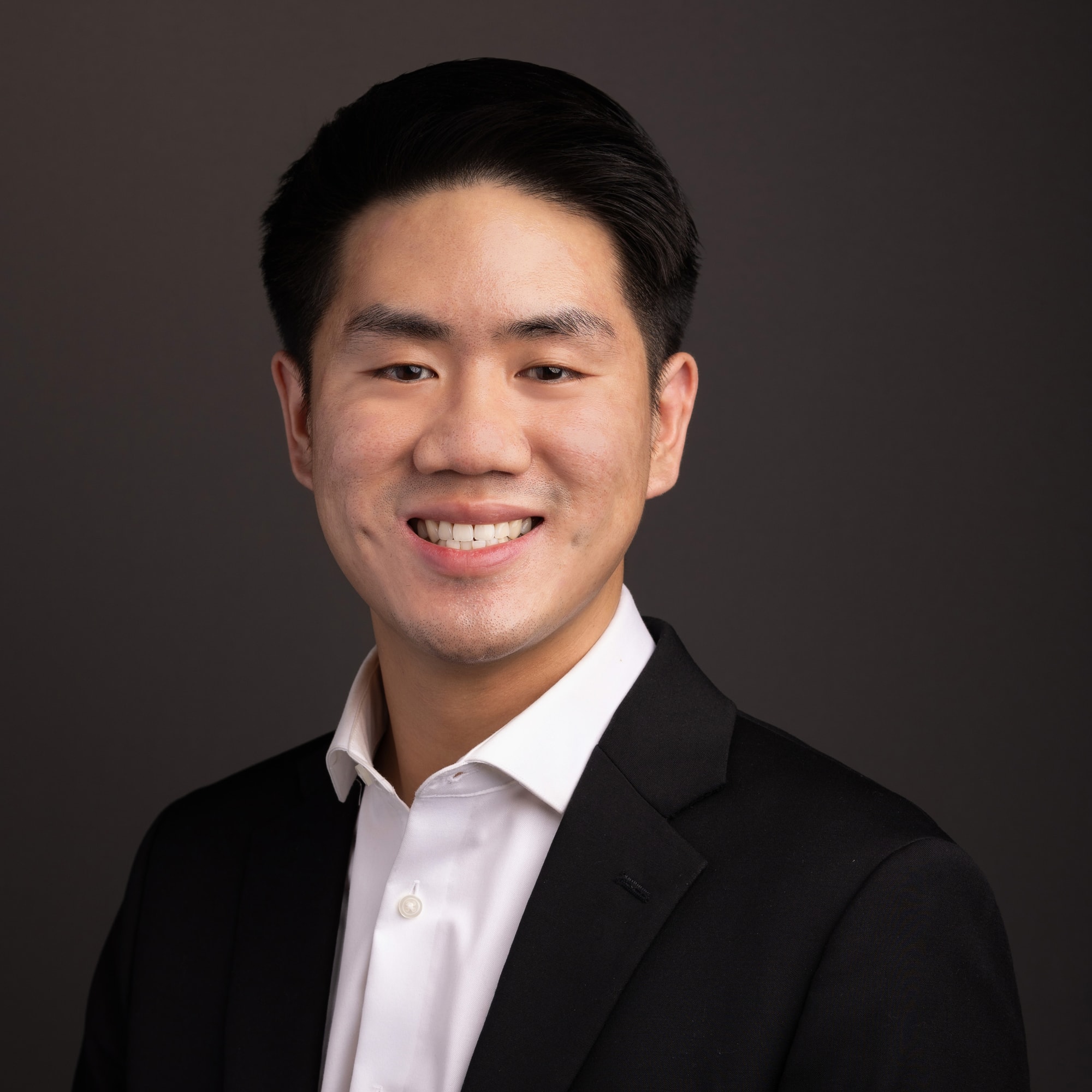 Studio headshot of Michael Lai, founder of Lai Collective, in a black blazer and white open-collar shirt